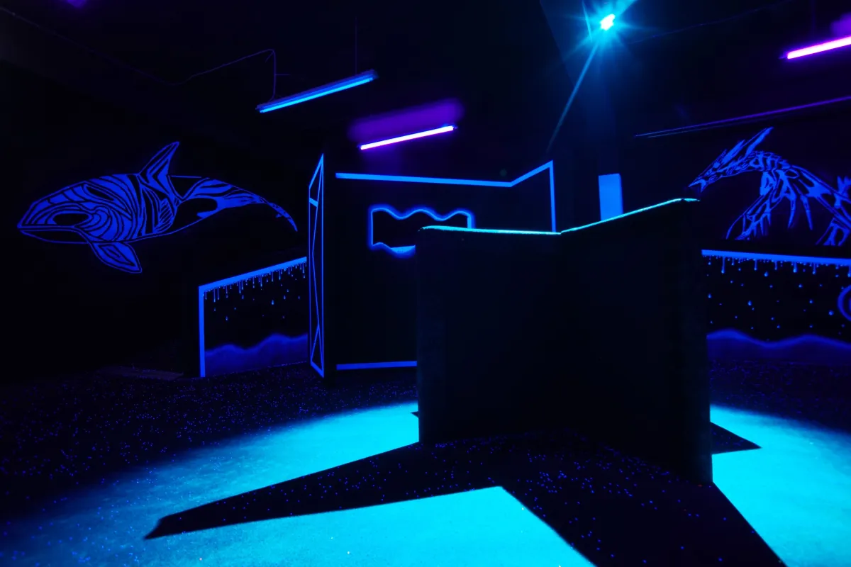Arenabereich mit blau-violetten Neonlichtern und Meerestier-Wandgemälden