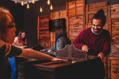 Gruppe spielt an einem Tisch in einem Raum mit Holzkisten